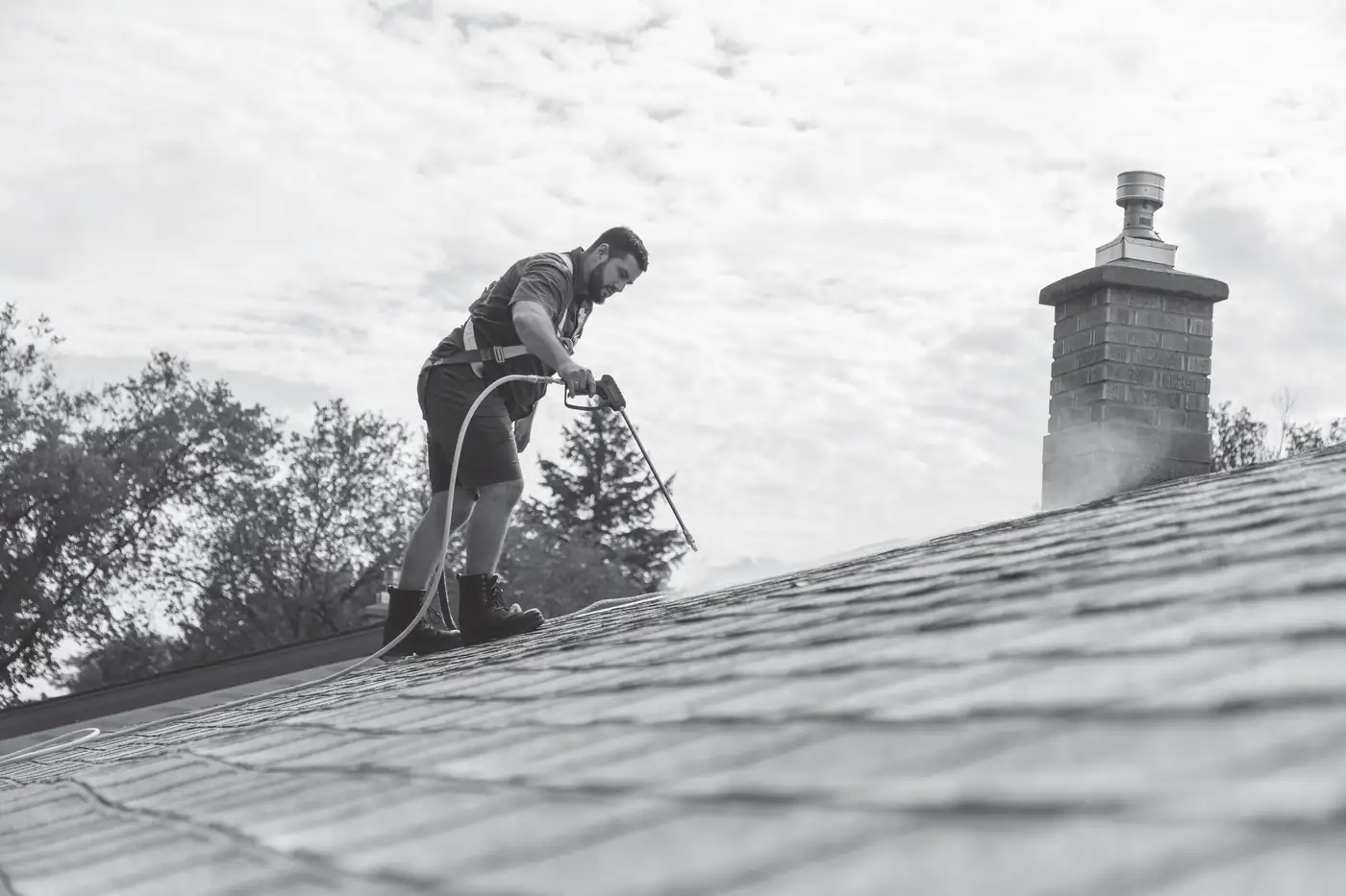 Technician spraying shingle treatment by a brick chimney, black and white