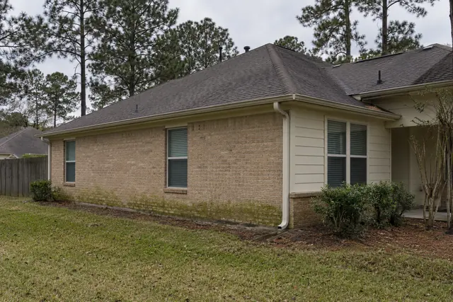 Tan brick and cream siding with green algae on the shaded wall of a one-story home